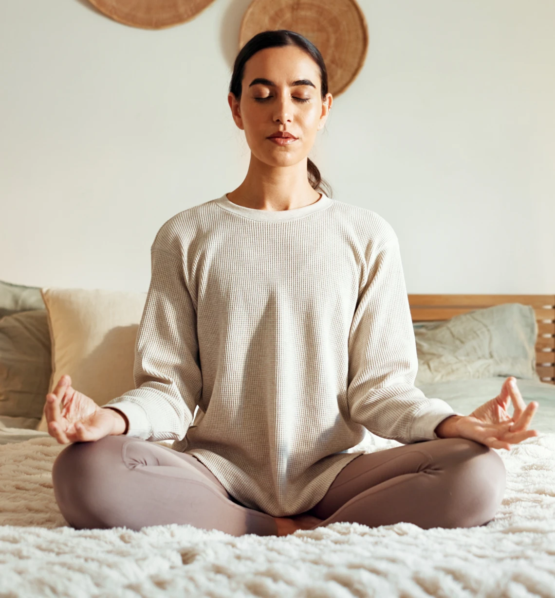 Woman meditating in a serene bedroom setting.