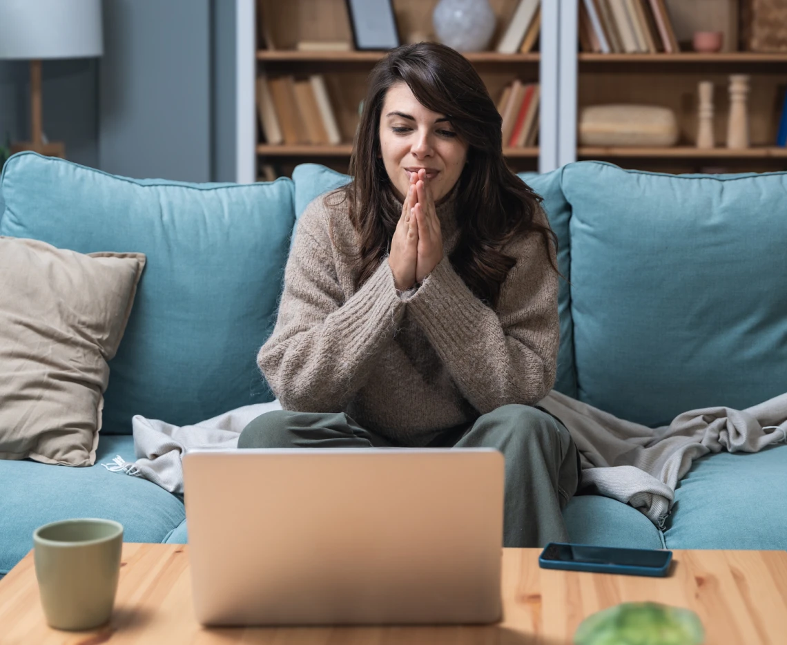 Woman smiling at laptop on cozy sofa.